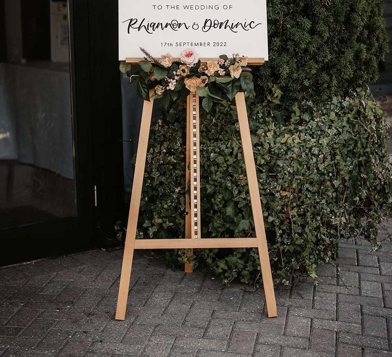 Luxe minimalistic welcome wedding sign on wooden easel with rose, peony, dried flower and foliage decorations 