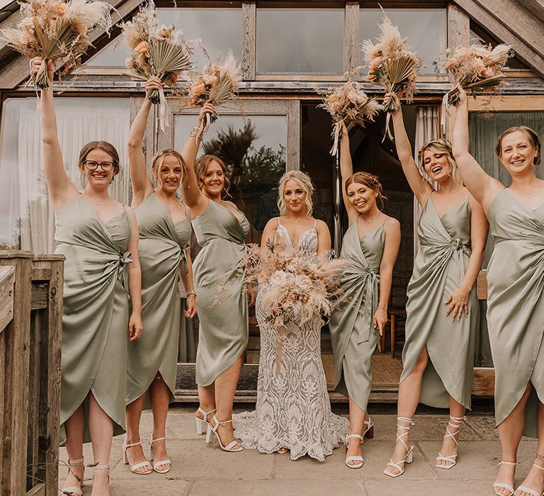 Satin sage green bridesmaid dresses worn by the bridal party holding pampas grass bouquets for the boho wedding with the bride in a Willowby by Watters dress