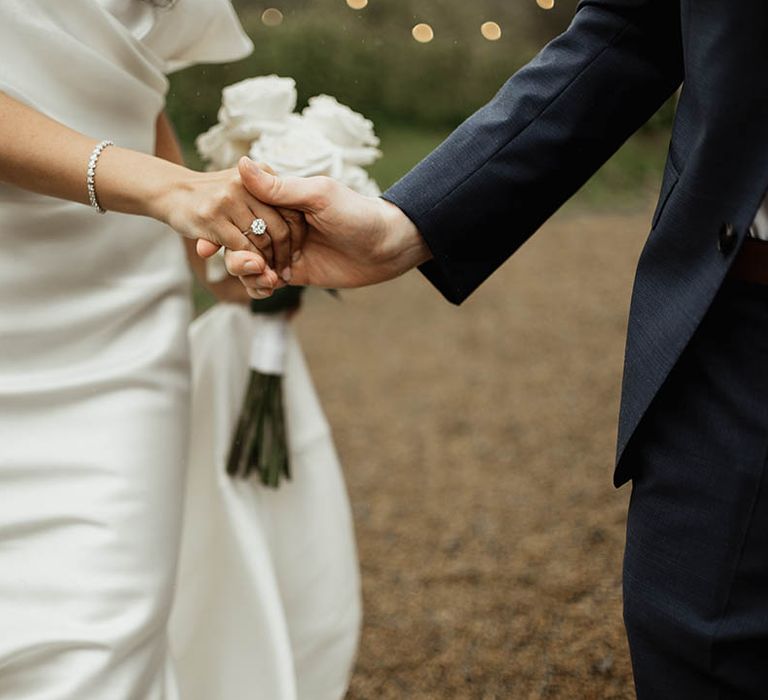 Bride holding a round white rose bouquet with a big round brilliant diamond engagement ring in an Eve Lendel wedding dress and diamond bracelet 