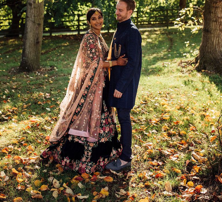 Bride wears beautifully embellished floral lehenga and embraces her groom outdoors during golden hour couples portraits 