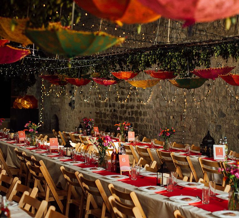 Banquet tables complete with white tablecloth and colourful table runners as Indian umbrellas hang above finished with fairy lights