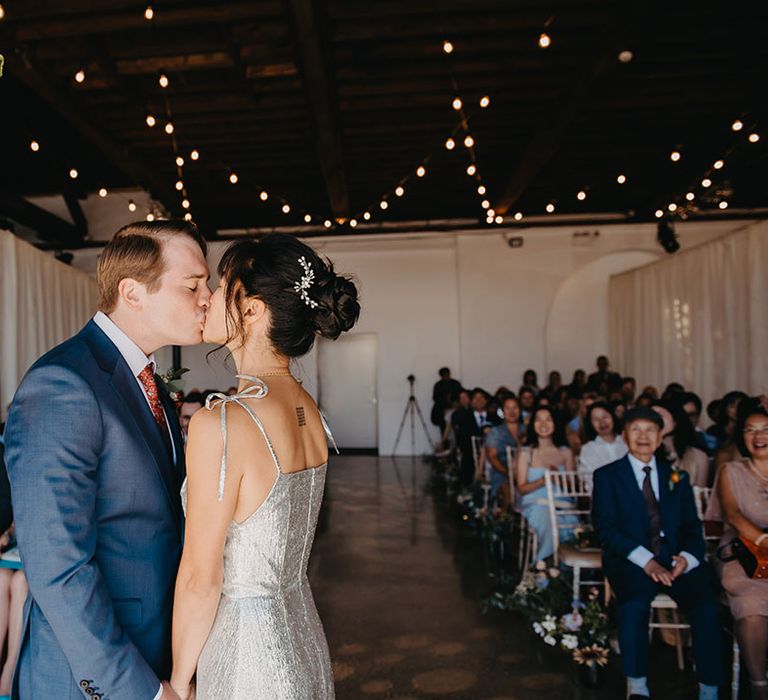 Bride in silver wedding dress kisses her groom during bespoke wedding ceremony 