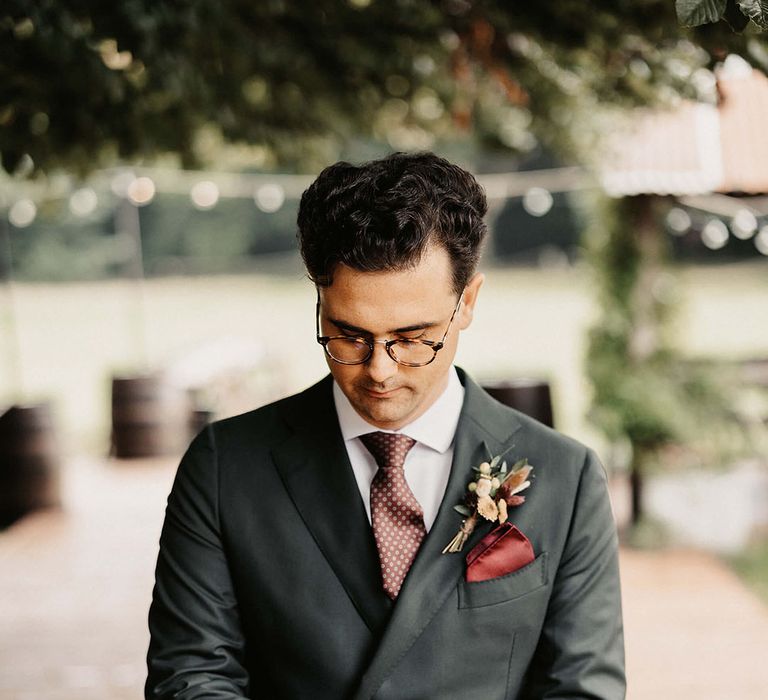 Groom wears bespoke Suit Supply suit complete with silk red pocket square and floral buttonhole