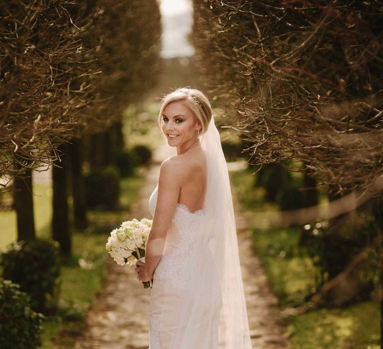 Bride in strapless lace mermaid gown for the wedding day with small white round bouquet 