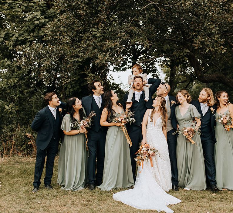 Wedding party photo with the bridesmaids in green TH&TH bridesmaid dresses and the groomsmen in navy suits with the bride and groom