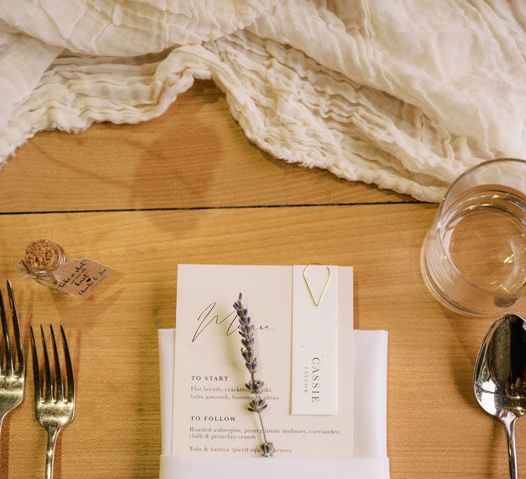 White wedding menu with wedding place name attached with gold paperclip with sprig of lavender and white napkin with silver cutlery