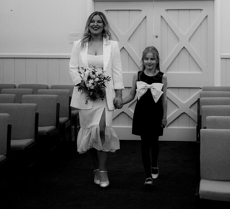 The bride and groom's daughter walks the bride in a ruffle wedding dress and blazer down the aisle 