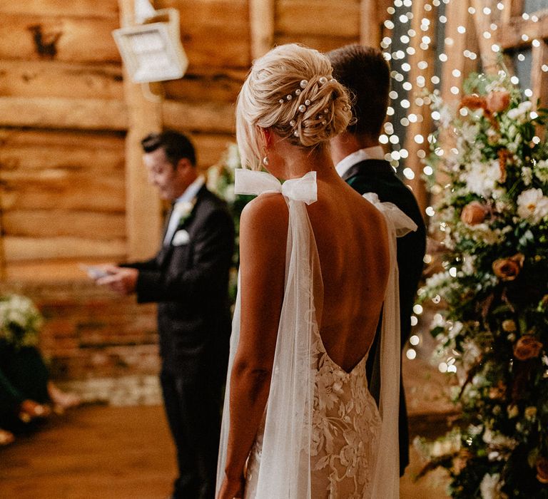 Bride wears her blonde hair in an updo decorated with pearl hair pins in a low back fitted lace wedding dress 