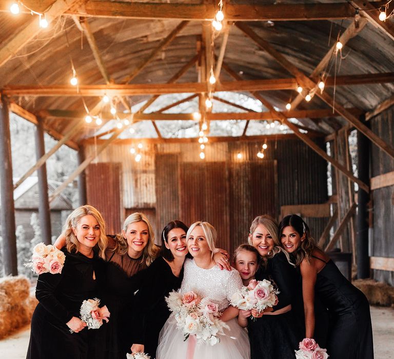 Bridesmaids in mismatched black bridesmaid dresses with the bride under the industrial shelter at Silchester Farm