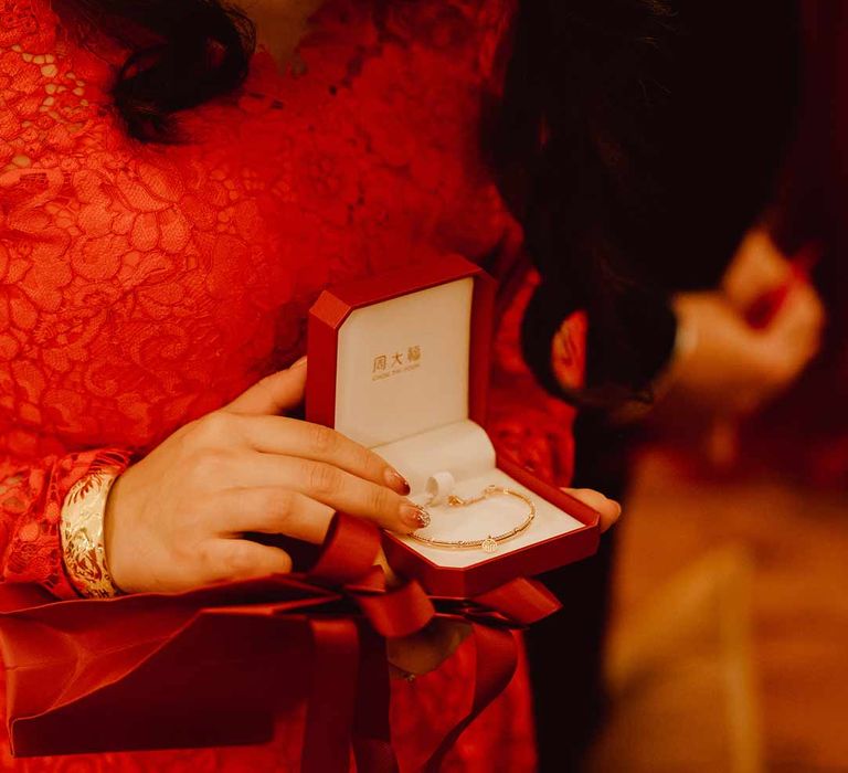 Bride in red lace wedding dress opening red velvet jewellery box to find gold wedding jewellery 