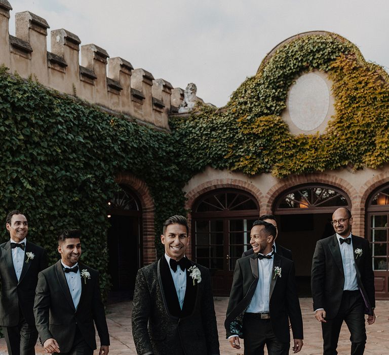 Groomsmen wearing matching black tuxedos with black bowties and white flower boutonnieres