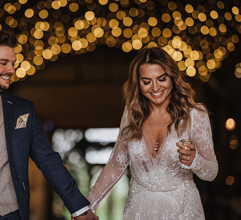 Groom in navy and brown suit and waistcoat with the bride in a long sleeve sparkly lace winter wedding dress walking out of their ceremony 