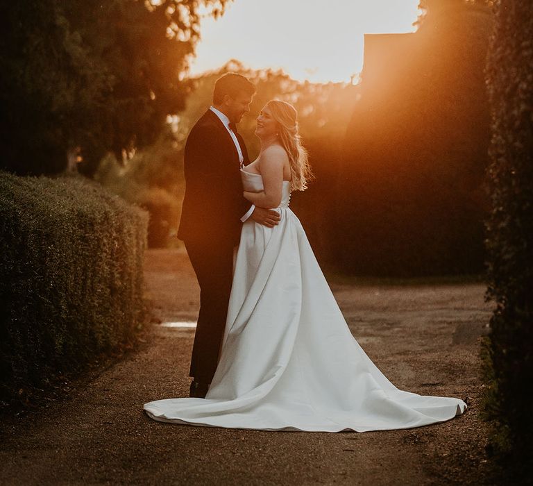 Golden hour wedding portrait of the bride in a strapless Suzanne Neville wedding dress and groom in black tie 