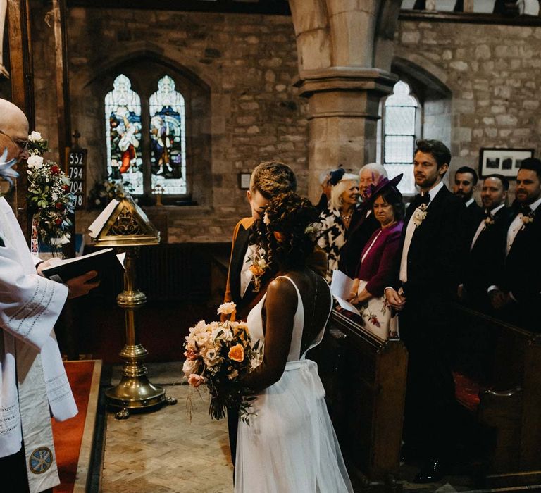 Bride standing with groom at alter wearing v-neck sleeveless wedding dress with 3D floral applique train 