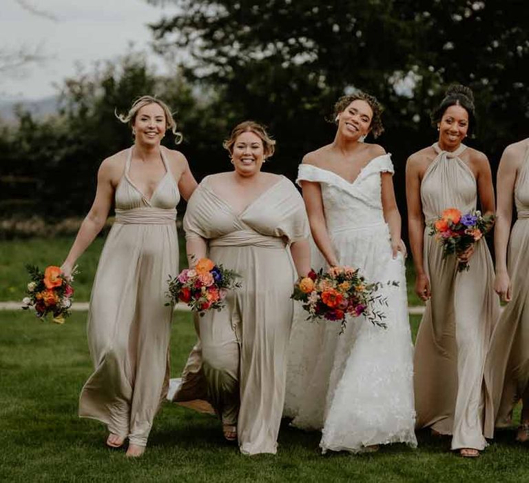 Bride in Suzanne Neville off shoulder 3D floral applique wedding dress walking with bridesmaids in multiway off-white bridesmaid dresses at Elmore Court Gloucestershire