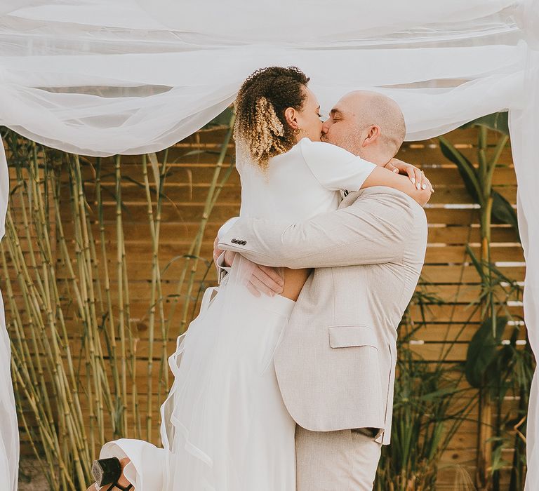 Groom in cream suit lifts the bride in emotional embrace at their Jewish humanist wedding ceremony 