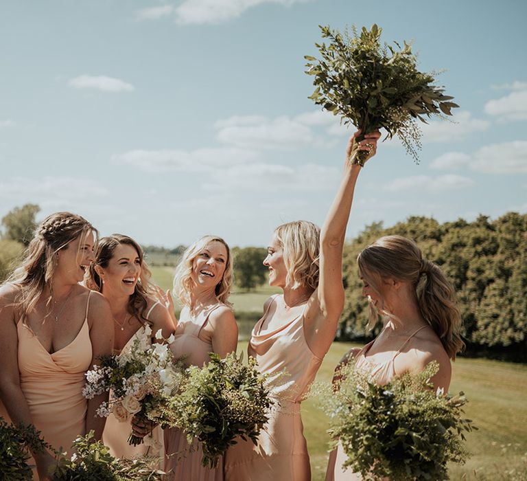 Bridesmaids in mismatched style bridesmaid dresses holding up their own green foliage bouquets 