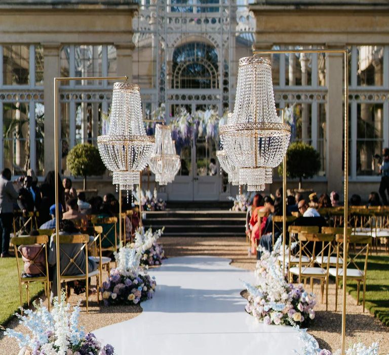 Syon Park wedding venue with outdoor gold and crystal chandeliers and pastel aisle flower arrangements outside of The Great Conservatory for vow renewal 