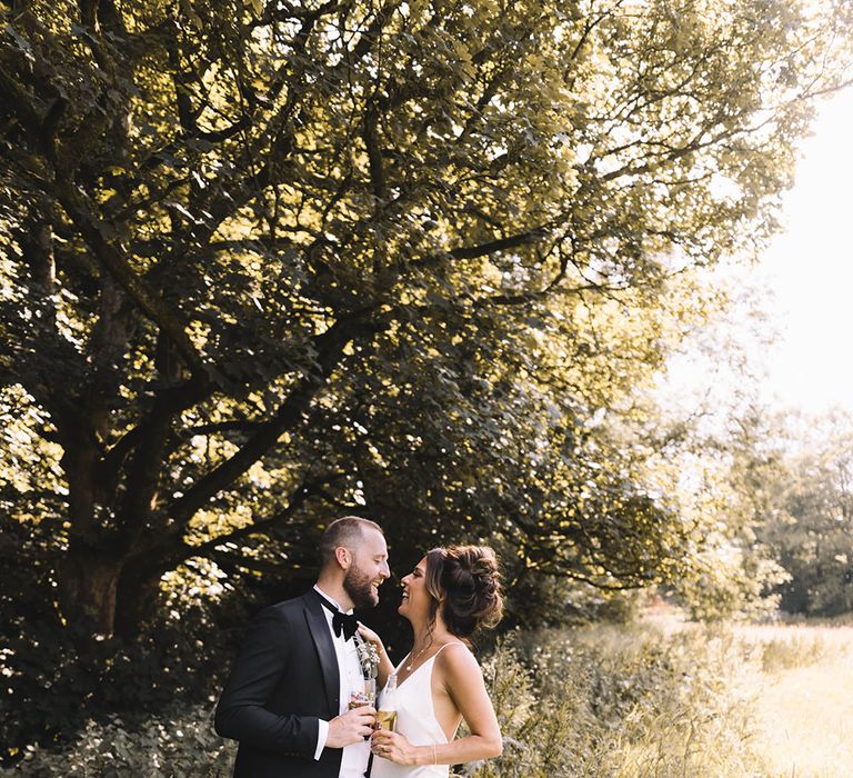 Bride in satin slip wedding dress kissing the groom for couple portrait as the sun starts to set