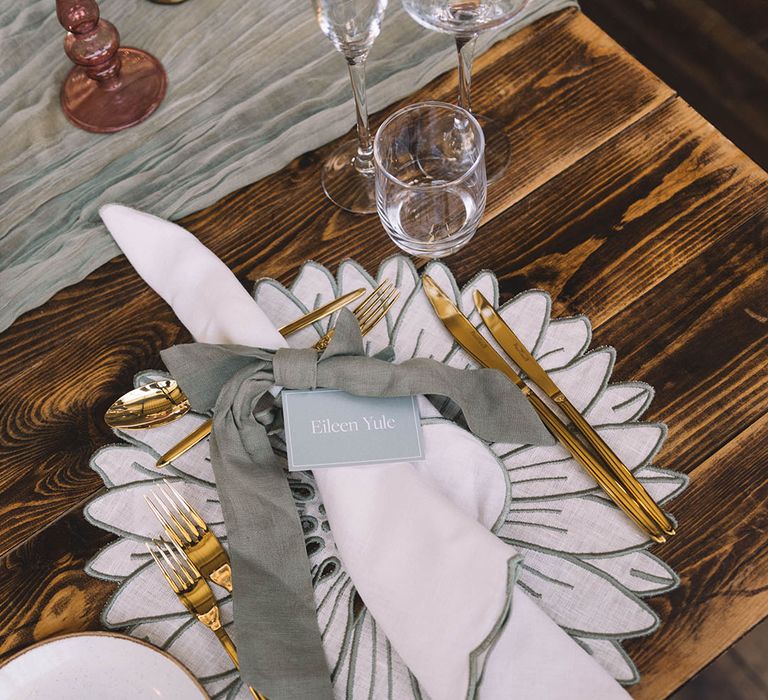 White and sage green floral place mat with gold cutlery, white napkin and place name 