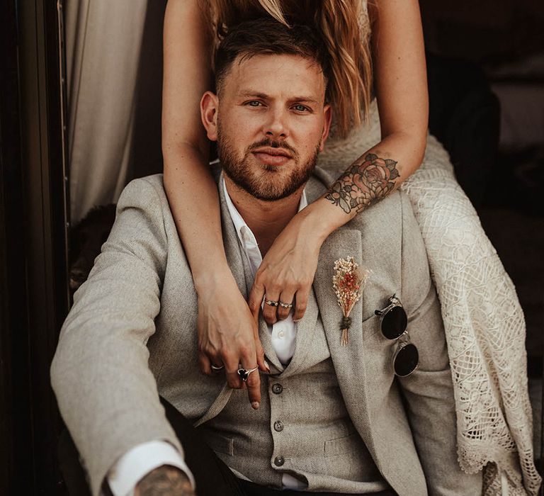 Groom wearing stone coloured wedding suit with dried flower buttonhole with the bride in a delicate lace wedding dress 