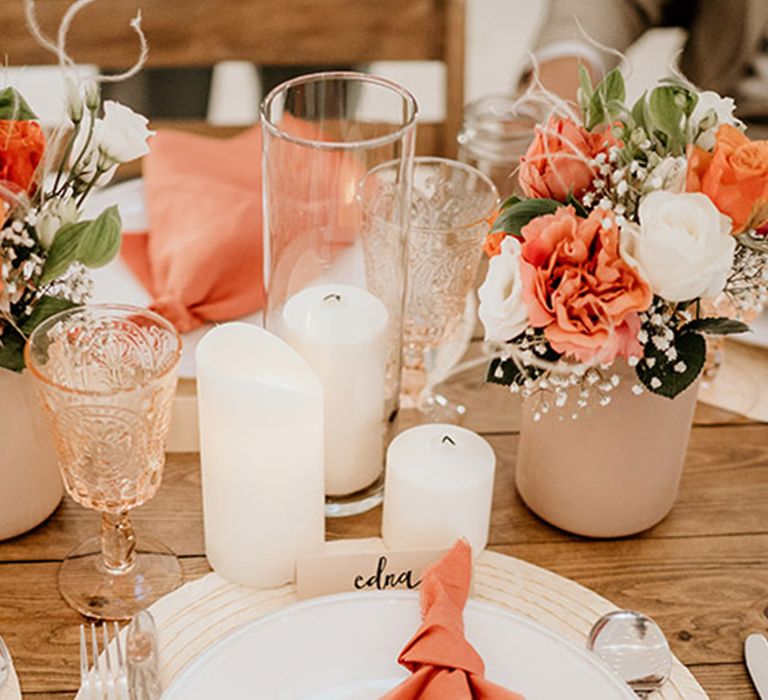 Coral and peach theme wedding place setting with a white placemat and plate with silver cutlery and peach napkin 