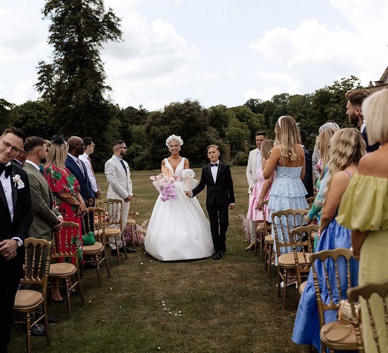 Bride walking down the aisle with her son at outdoor wedding ceremony 