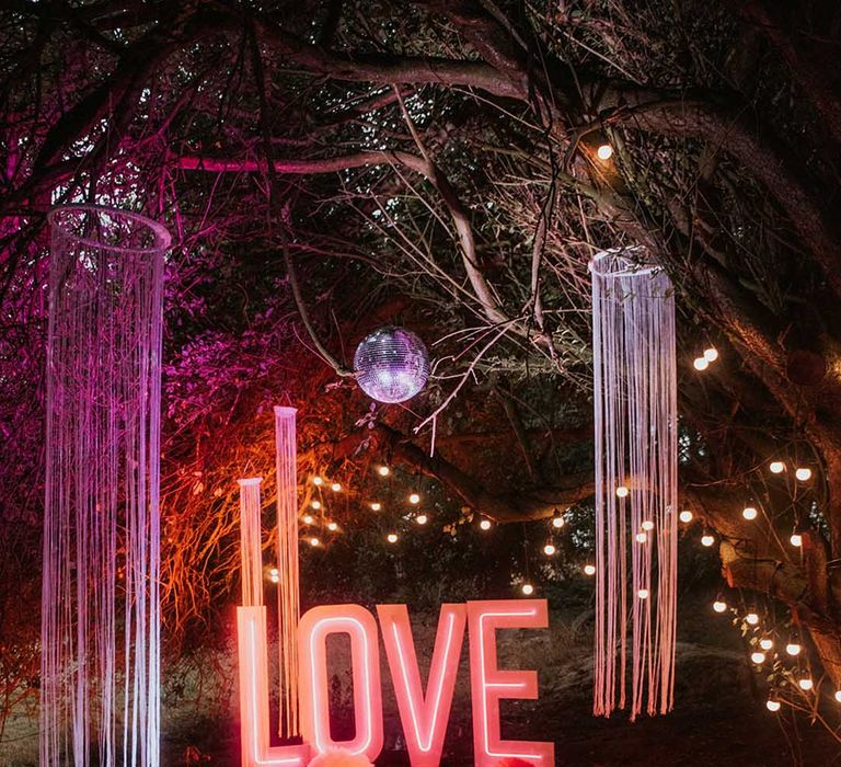 Large neon sign spelling out 'Love' with hanging lights at outdoor area