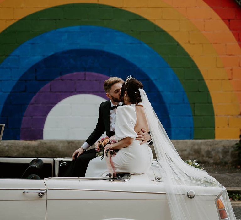 Bride and groom kiss in white vintage wedding car 