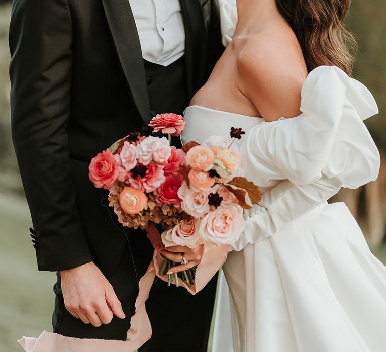 Bride with sparkly hair piece holding autumnal bouquet leaning in for a kiss with the groom 