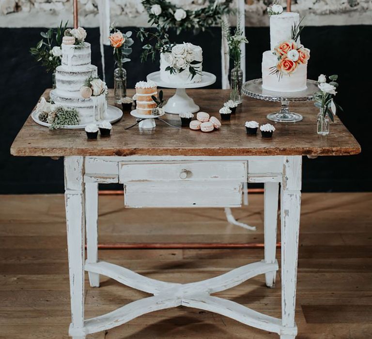 Wooden dessert table with three rustic wedding cakes with cupcakes decorated with white frosting and macarons 