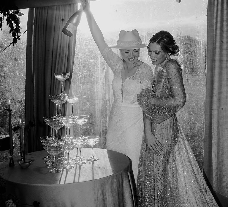 Two brides in wedding reception outfits with champagne tower 