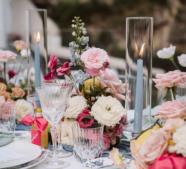 Pink, yellow and blue wedding tablescape decorations with blue taper candles, pearl napkin holders and pastel flower centrepieces 