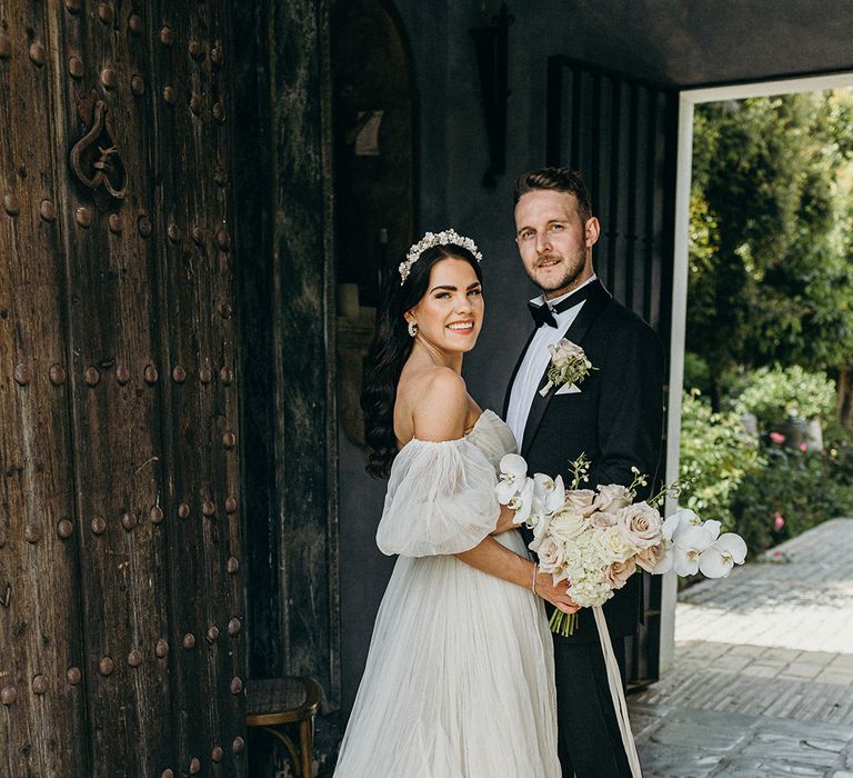 Bride in classic off the shoulder wedding dress with groom in black tuxedo for traditional black tie Hollywood glam wedding 