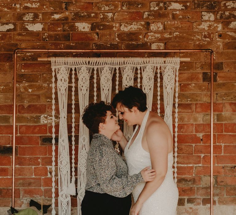 LGBT Wedding with two brides standing in front of a macrame backdrop