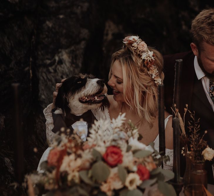 Doggy in a bow tie and suit celebrates with boho bride in a flower crown and groom with a floral tie