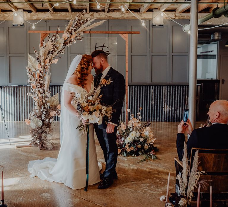 Bride and groom standing at the wooden altar decorated in dried flowers 