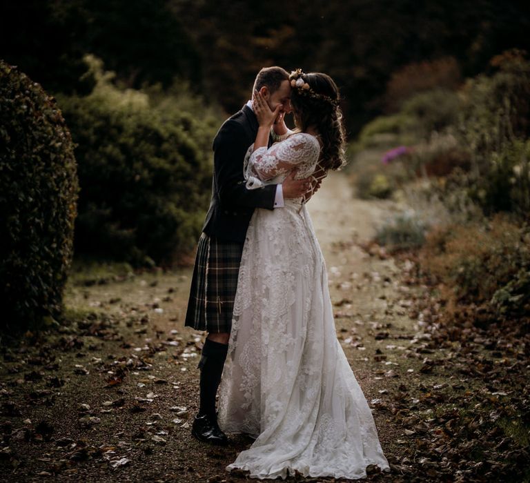 Boho bride with rose flower crown kisses groom in gardens at highland wedding in Glencoe