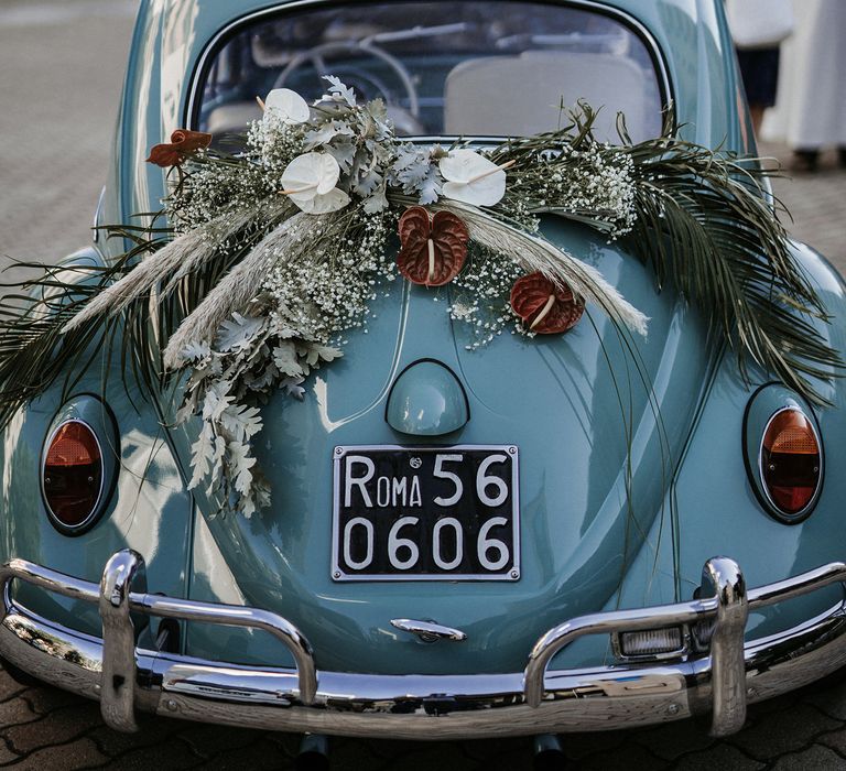 Blue Volkswagen Beetle with dried flower arrangement decorating the back 