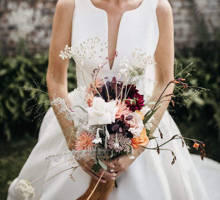 Blonde bride with a fringe in a wedding dress with plunging neckline holding a wildflower wedding bouquet 