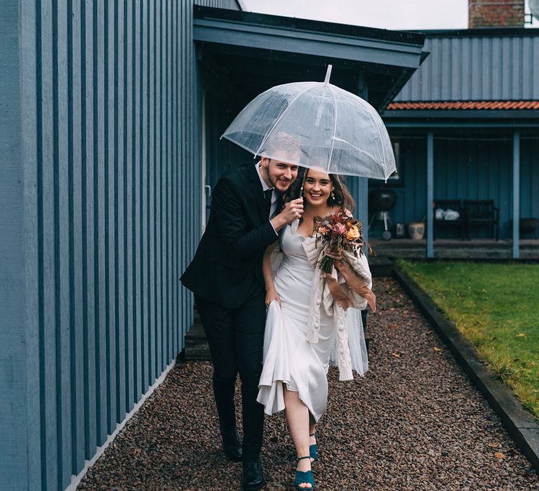 The bride and groom running through the rain with an umbrella