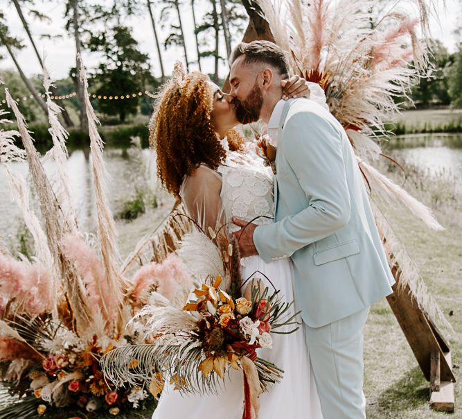 Bride & groom kiss during ceremony surrounded by pampas grass and wooden arch