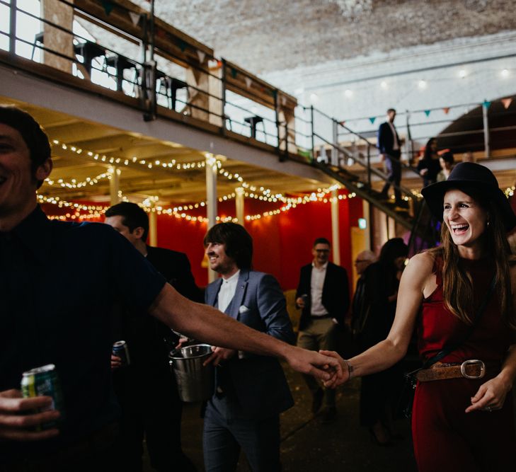 Wedding guest laughing, wearing red dress and black hat in a hall with hanging lights