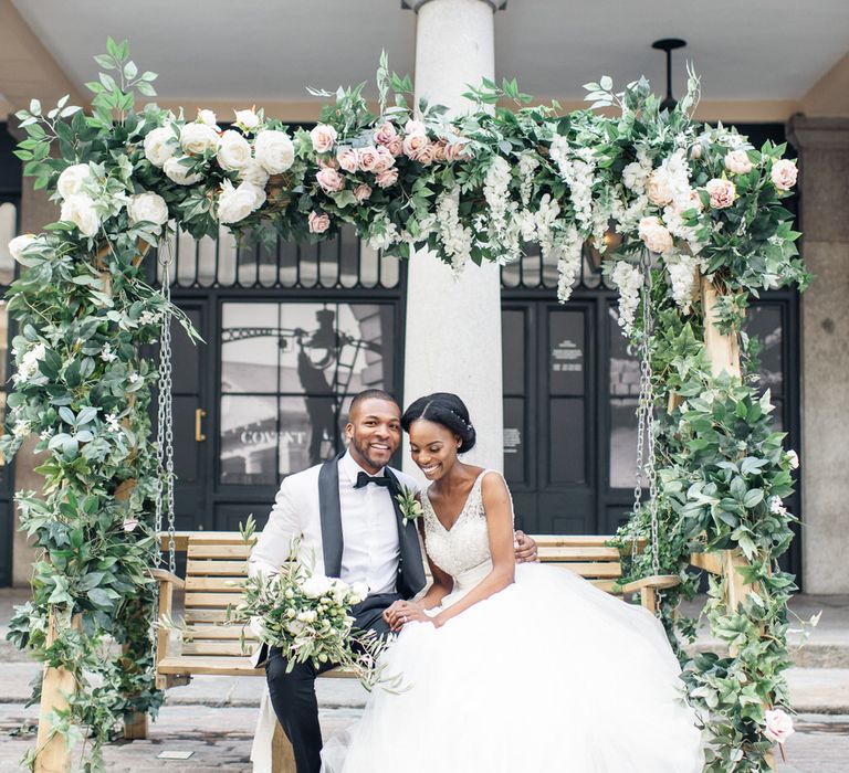 Bride & groom sit beneath floral arch in Covent Garden