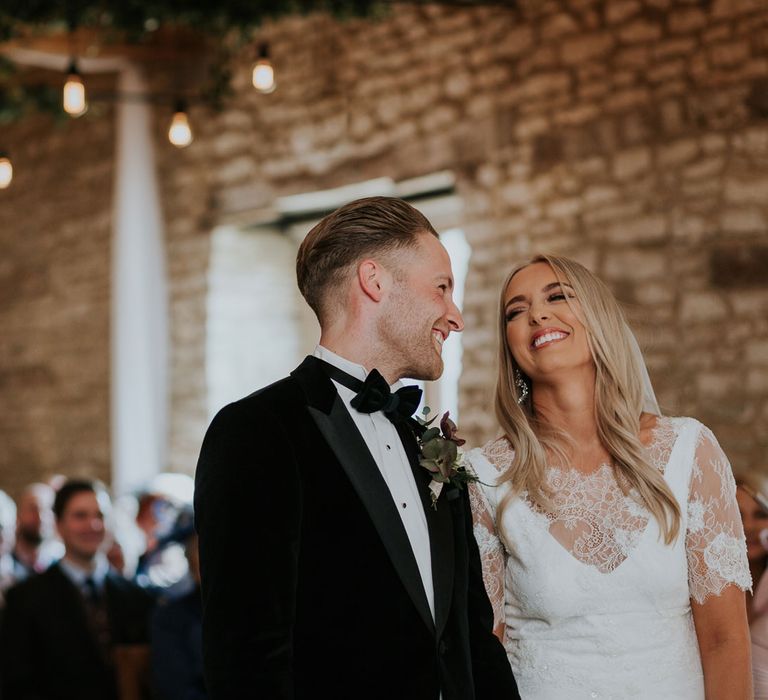 Bride in white Charlie Brear wedding dress and white Augusta Jones lace top and groom in black velvet Hugo Boss suit laugh together at Caswell House wedding