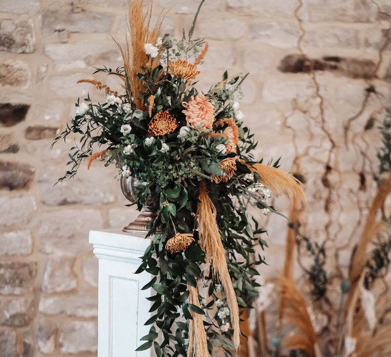 Orange and green foliage floral arrangement on a plinth 