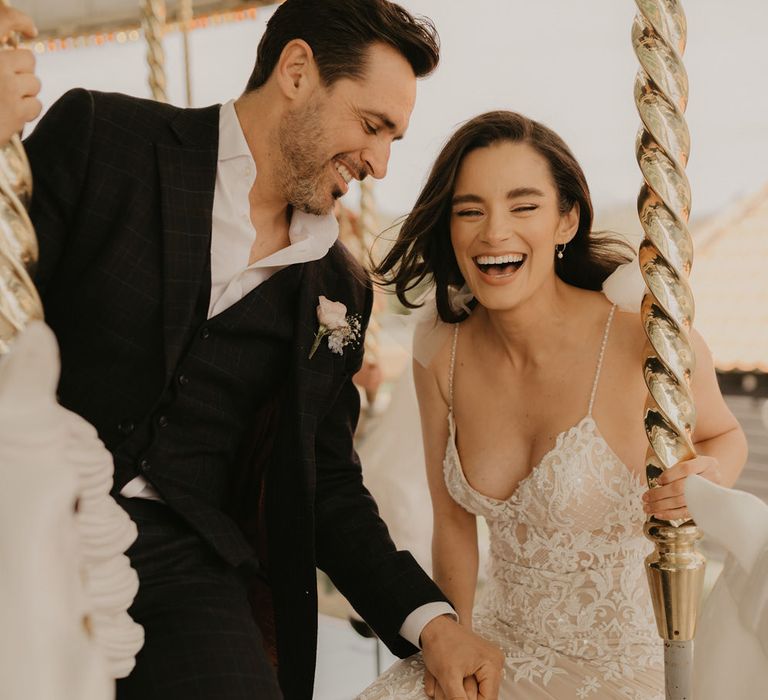 Bride and groom in a black suit and lace dress riding the carousel at Preston Court 