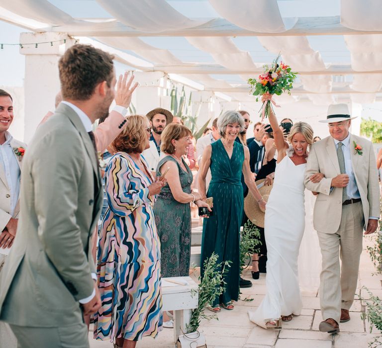 The bride cheers as she walks up the aisle arm in arm with her father