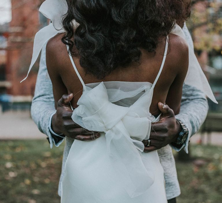 Groom with his hand on the back of bride's white satin Bec + Bridge wedding dress with tulle bow detail