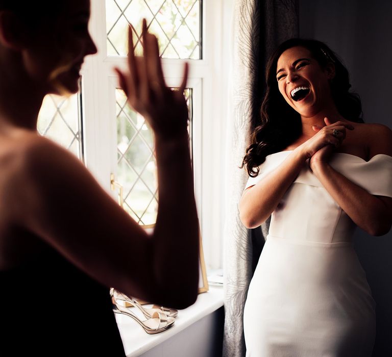 Bride in strapless Vagabond wedding dress laughs and clasps hands at lusher in black strapless dress and curled ponytail